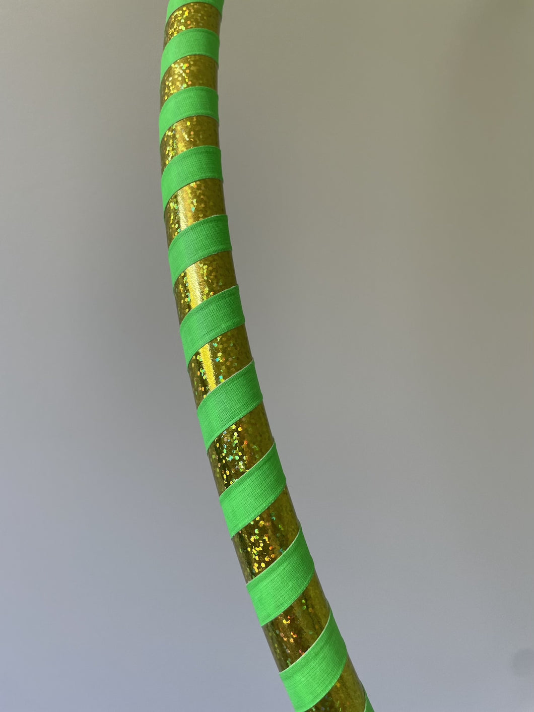 Hula hoop for beginners with gold and green striped pattern on a plain background