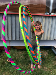 Woman holding 3 hula hoops, one beginner 3 colour hula hoop, one lime green hula hoop and one neon orange and teal small hula hoop all made for adults in nz